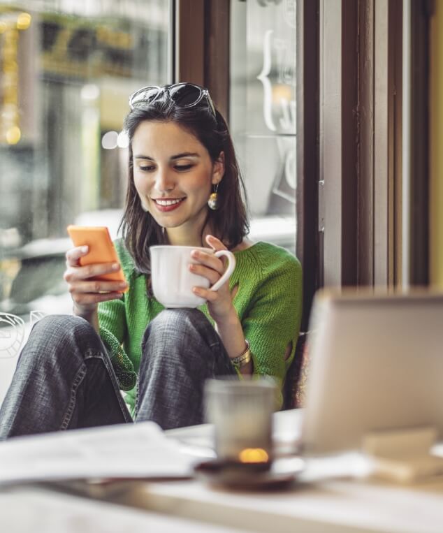 woman smiling at phone holding coffee mug